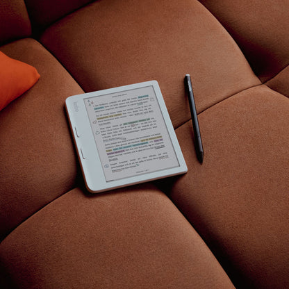 Kobo Libra Colour 7" sort e-bogslæser med E Ink Kaleido 3 skærm og sort stylus på brun pude ved orange hovedpude.