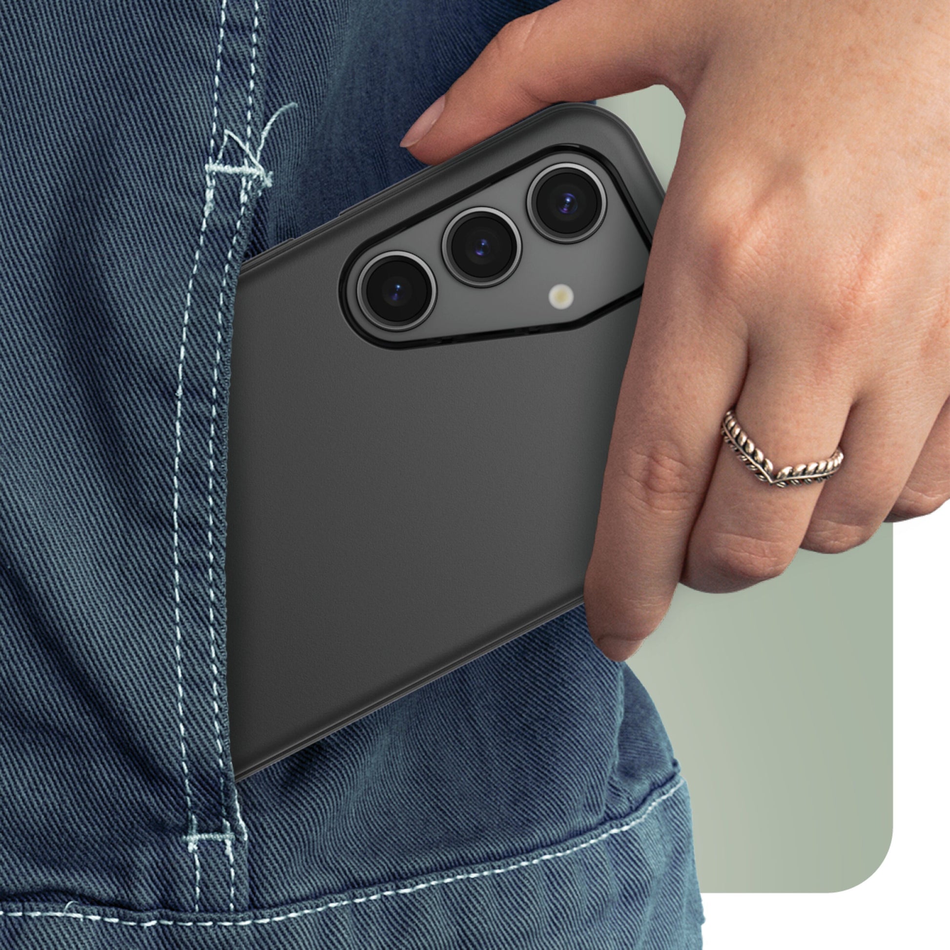 Galaxy S24 sort med tre bagkameraer i Robustt etui, delvist i blå denim jeans, hånd med sølvring.