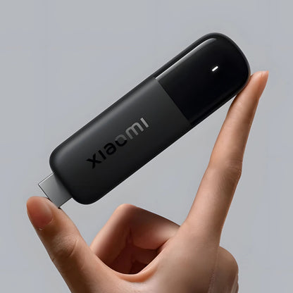 Xiaomi TV Stick 4K 2. gen sort balanceret på en finger, tydeligt produkt med logo synligt mod grå baggrund.