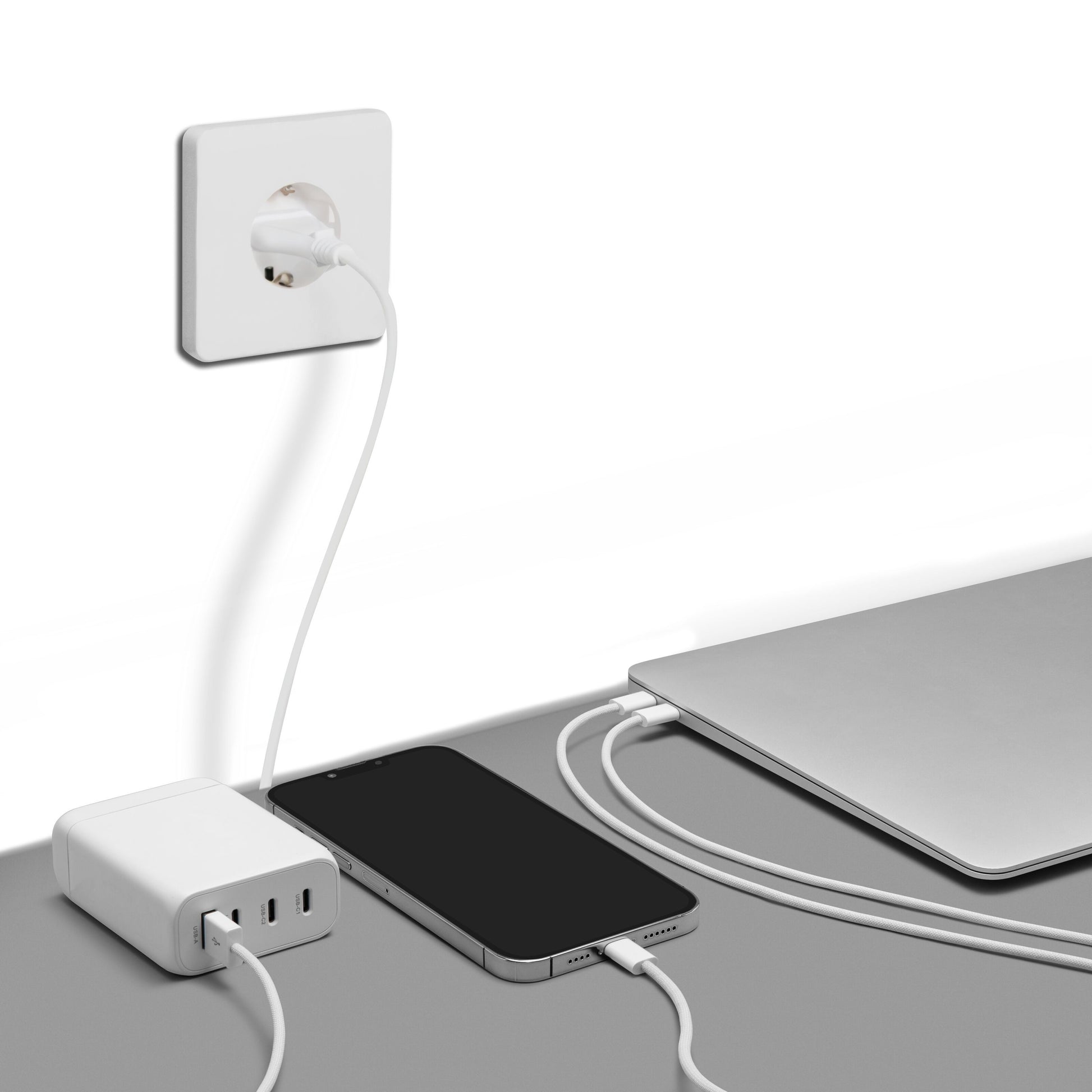 Premium GaN Multilader PD 3.0 100W hvid oplader smartphone og laptop via hvide kabler fra stik i grå bordplade.