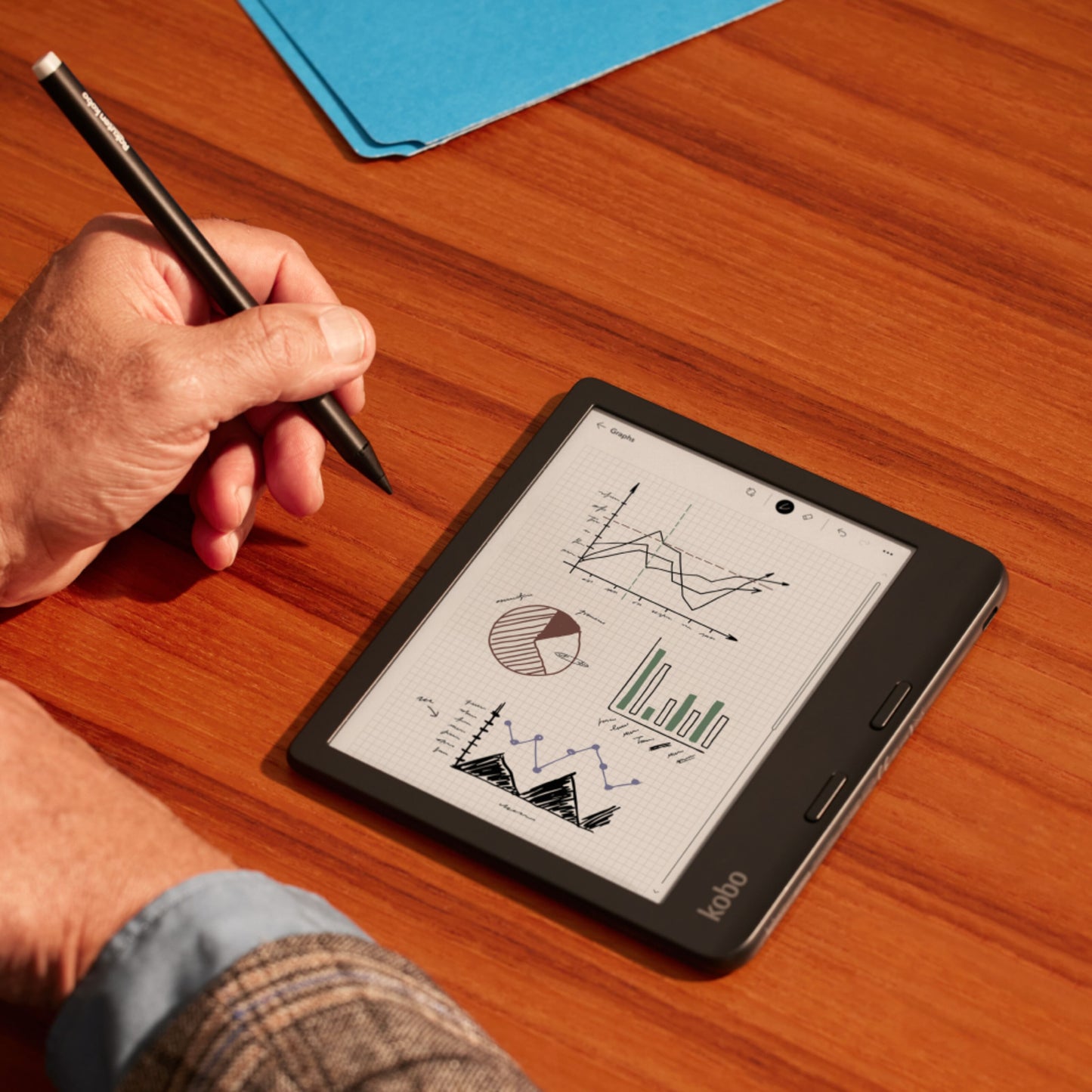 Kobo Stylus 2-pen Hvid bruges med e-læser, skærm viser grafer og diagrammer, blå mappe delvist synlig i baggrund.