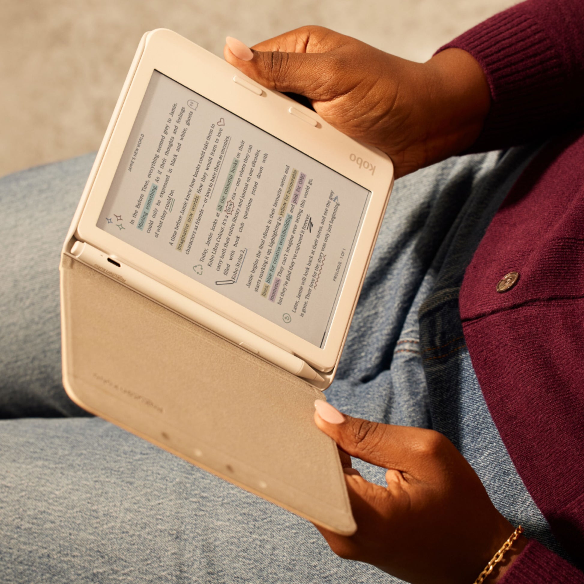Kobo e-reader med beige cover og Kobo Stylus 2-pen Hvid i brug, bæres af person iført blå jeans og bordeaux sweater.