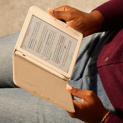 Kobo e-reader med beige cover og Kobo Stylus 2-pen Hvid i brug, bæres af person iført blå jeans og bordeaux sweater.