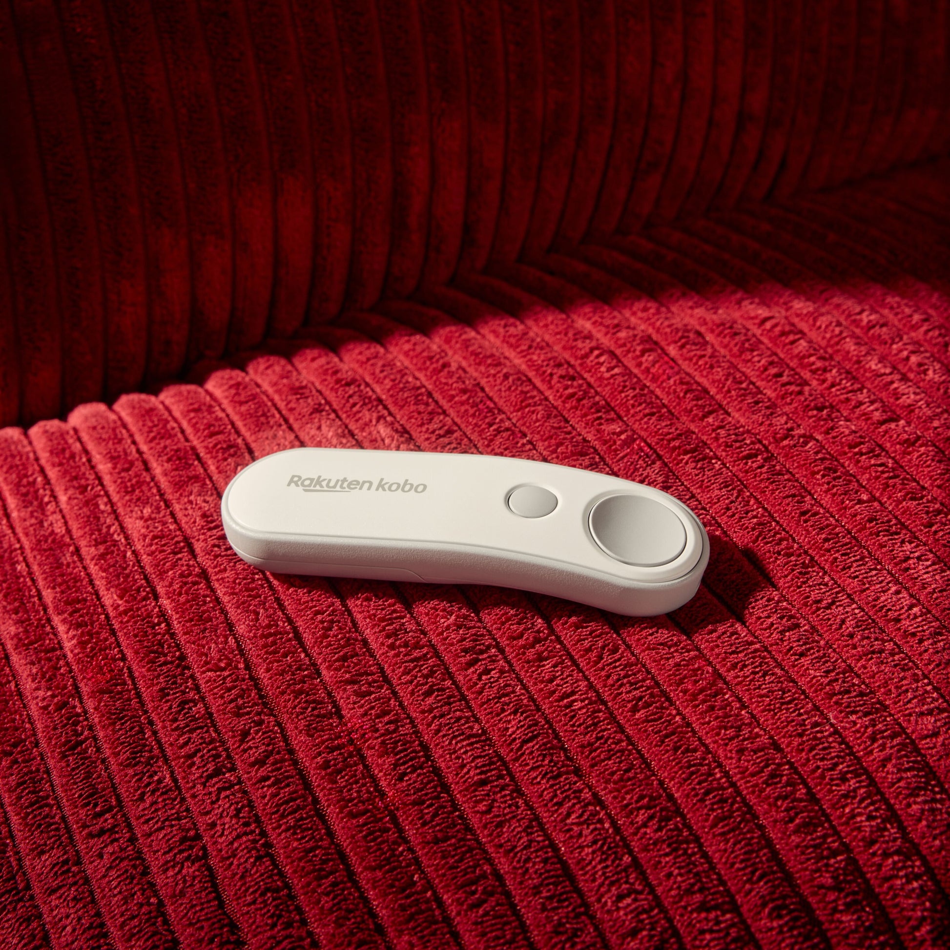 Kobo Trådløs sideomskifter med to knapper til Kobo e-læser, vist på rød fløjlsstof sammen med en Kobo e-læser.