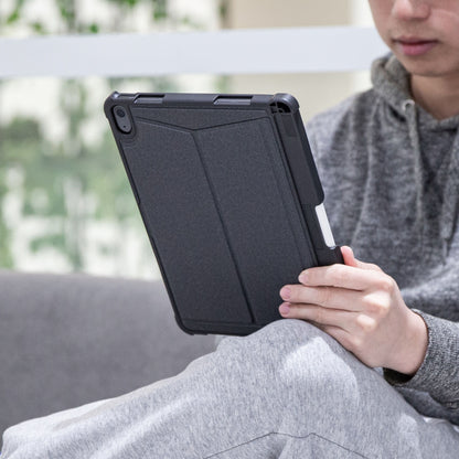 IPad 10,9" Gen. 10 i sort tastaturcover med Bluetooth-tastatur holdes i hænder, sofa og grøn baggrund anes.