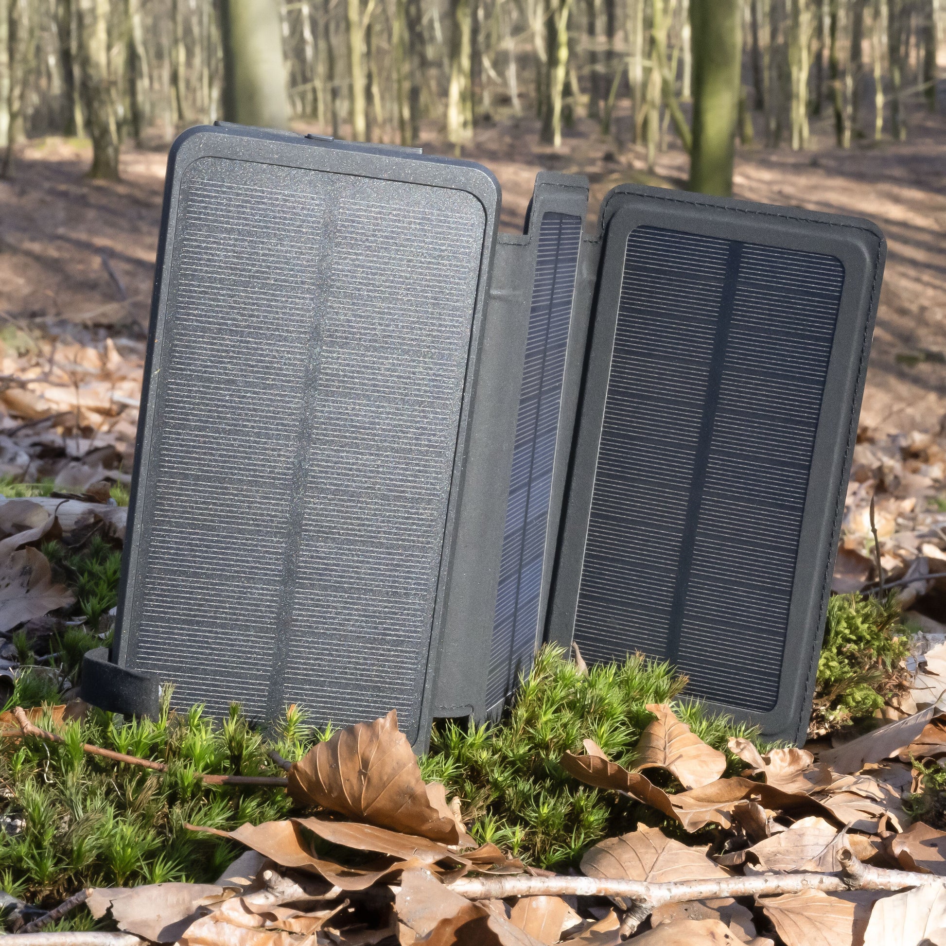 Linocell powerbank med solcelle, sort, 20 W 8000 mAh åben på mos i skov omgivet af blade og træer.