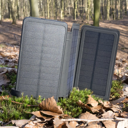 Linocell powerbank med solcelleopladning 30 W 16000 mAh åben på mos med tørre blade i solskov.