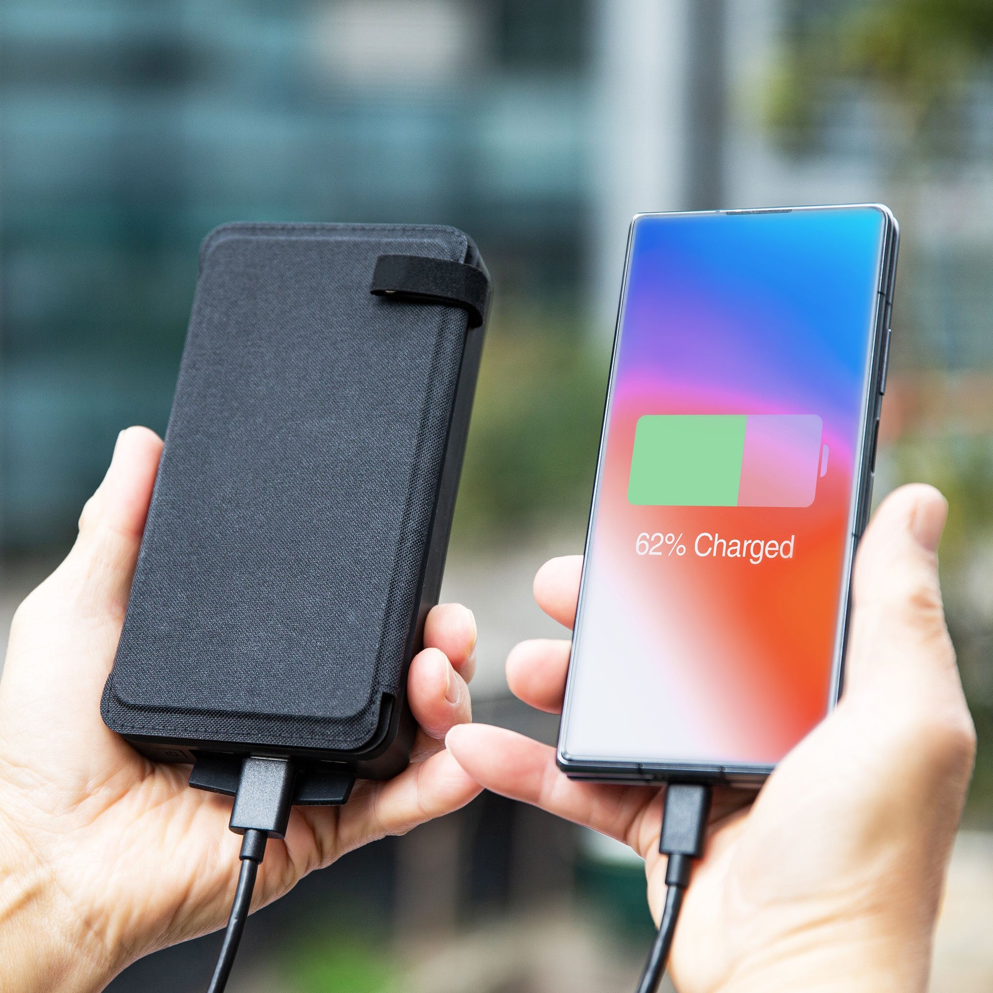 Linocell Powerbank med solcelle, 30W 16000mAh, tilsluttet smartphone med 62 batteri, udendørs baggrund sløret.