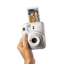 Fujifilm Instax Mini 12 kamera i hånden mens det udskriver et foto af to personer der smiler.