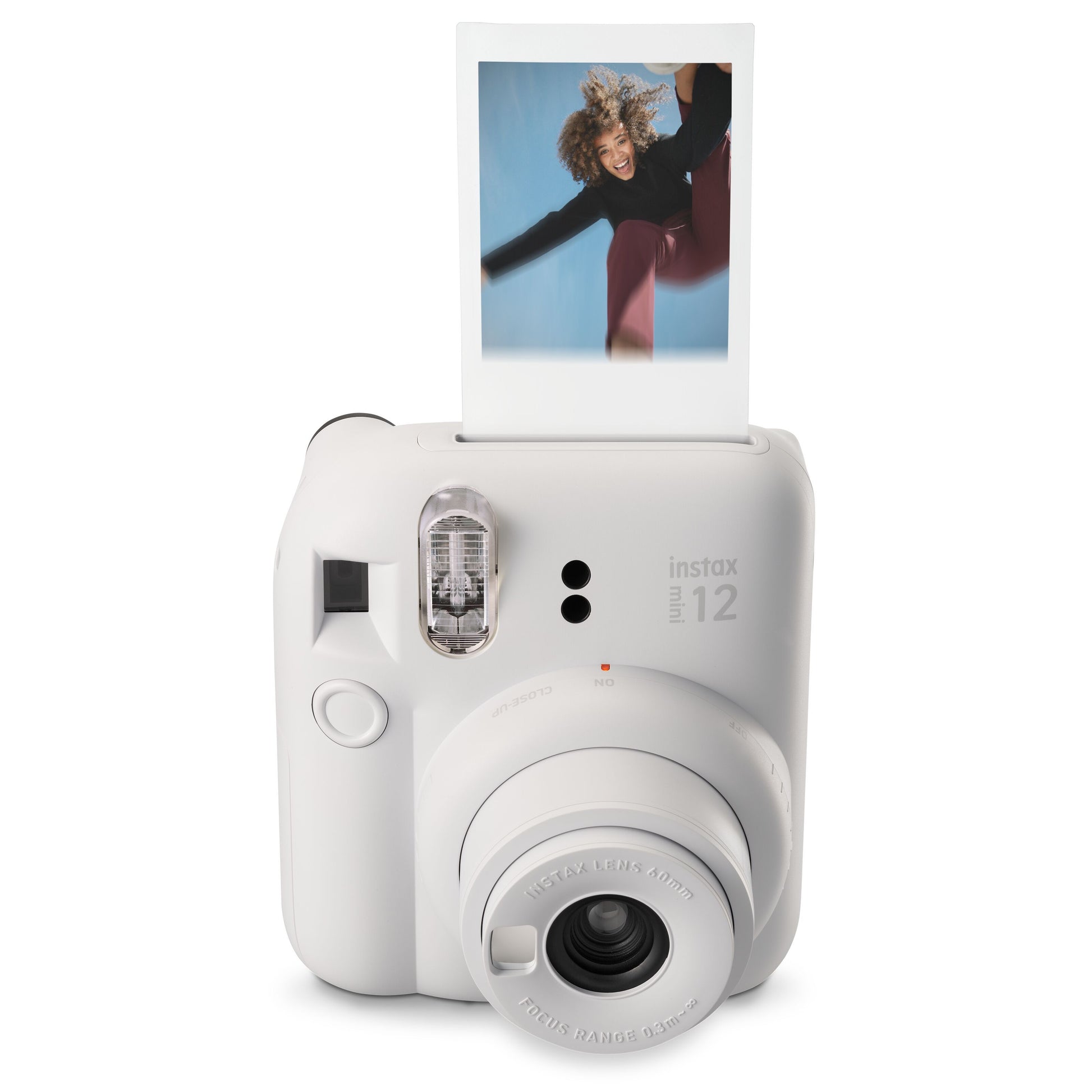 Fujifilm Instax Mini 12 kamera hvid, synlig søger og objektiv, viser øjebliksbillede med person under blå himmel.