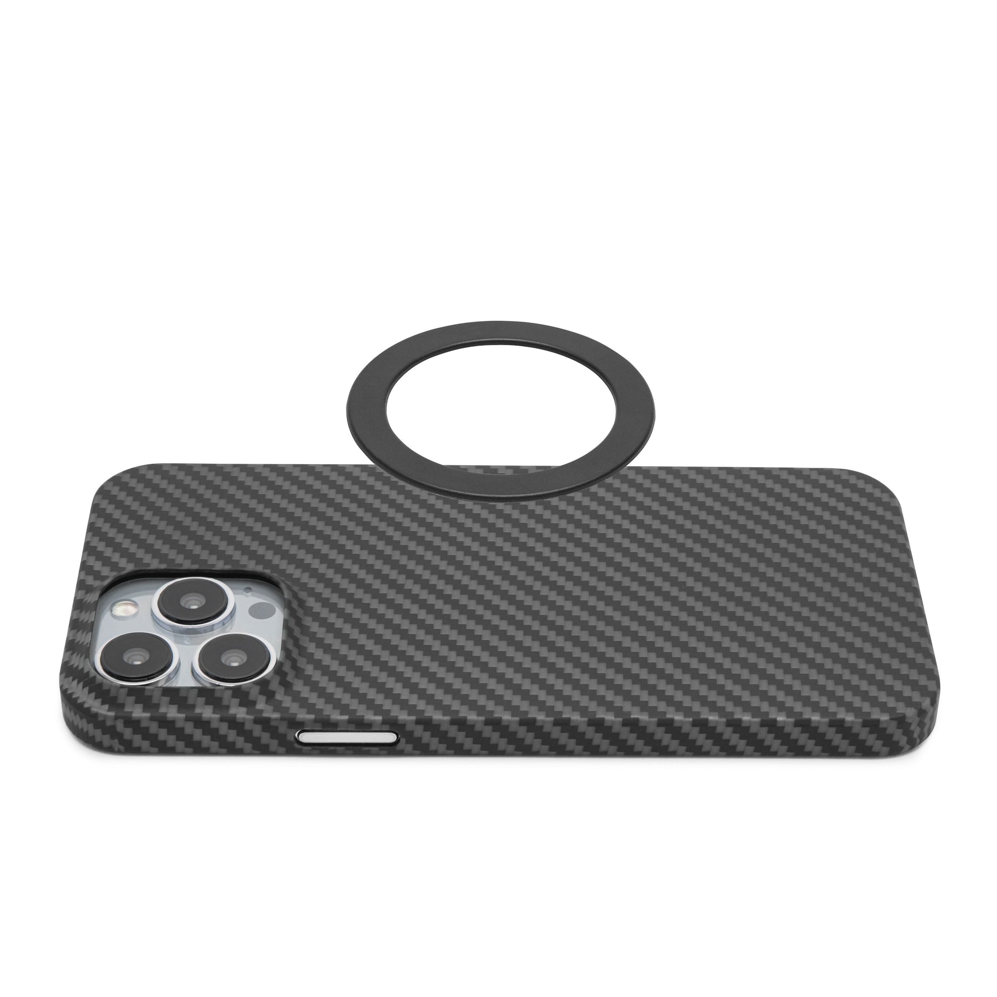 Smartphone med sort carbon cover, bagside opad, ved siden af rund sort Magnetisk adapter til trådløs opladning.