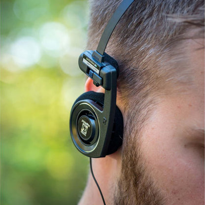 Koss Porta Pro 3.0 on-ear headset sort med skumpuder og indbygget mikrofon bæres over højre øre, udendørs baggrund.