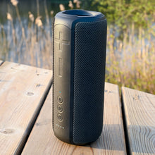 Nomadelic Loud 707 trådløs højttaler sort med store volumeknapper, Bluetooth 5.0 og IPX7, placeret på udendørs træbord.