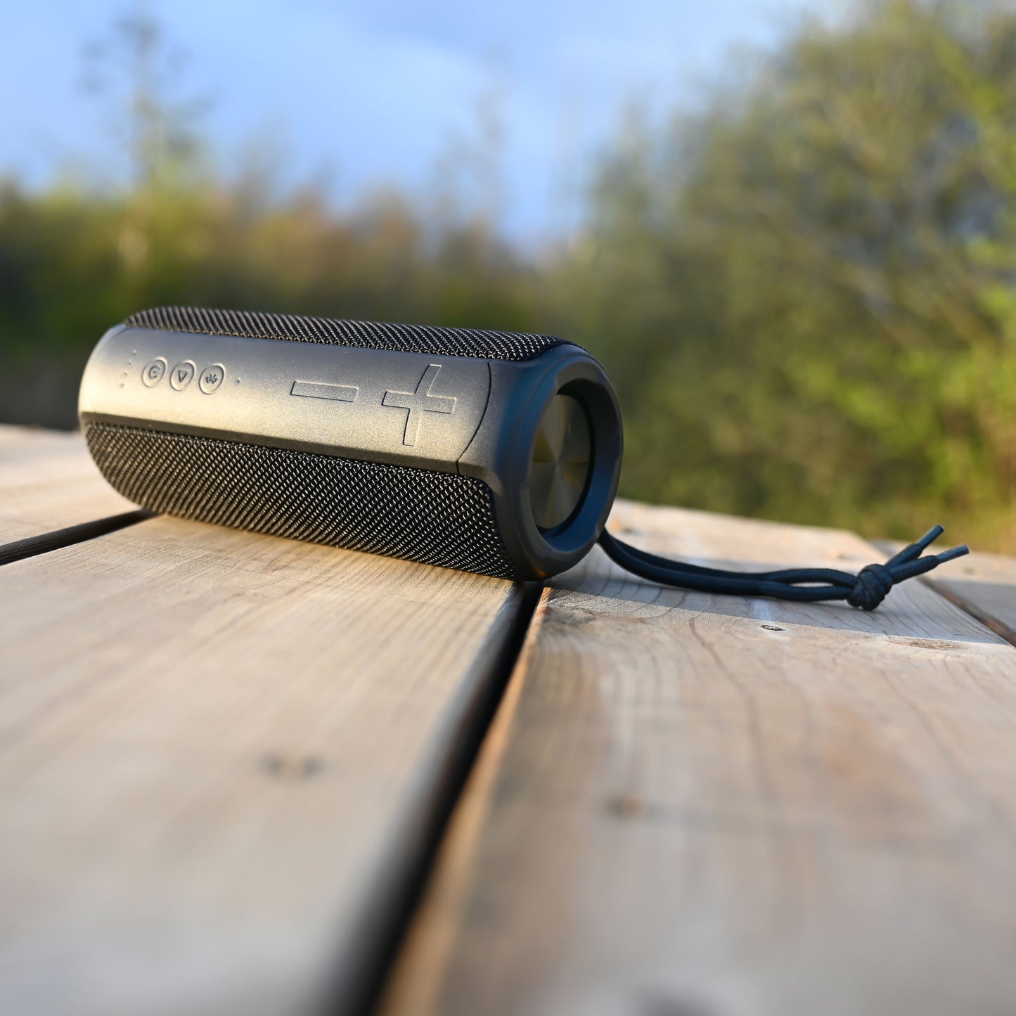 Nomadelic Loud 707 trådløs højttaler sort, Bluetooth 5.0, IPX7 vandafvisende, placeret på udendørs træbord.