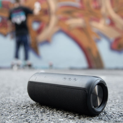 Nomadelic Loud 707 trådløs højttaler sort, Bluetooth 5.0, IPX7-vandafvisning, placeret udendørs foran graffitivæg.