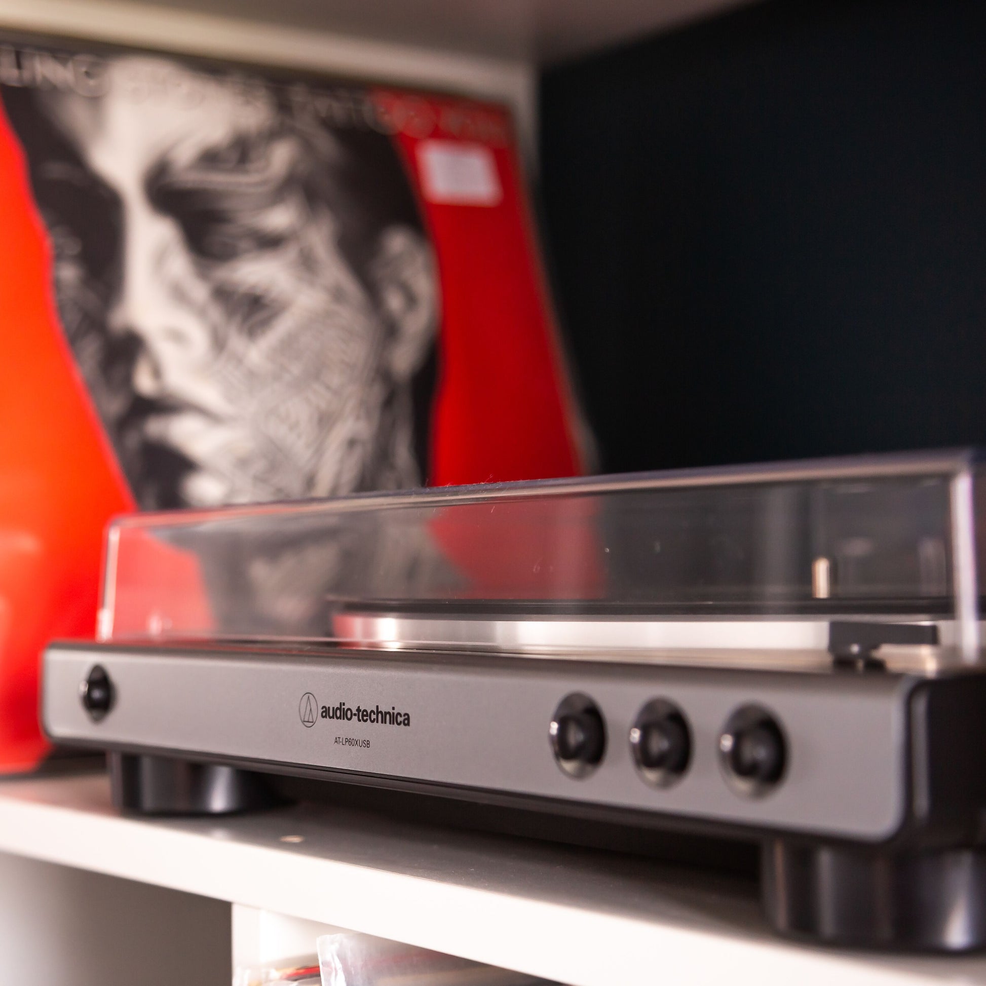 Audio Technica AT-LP60XUSB sort vinylafspiller med gennemsigtigt låg, rød vinyl med ansigtstegning bagved.