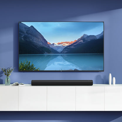 Xiaomi Soundbar 2.0 30W sort under vægmonteret TV med bjergsø-billede, hvidt skab, blomster og hvide objekter ved siden af.