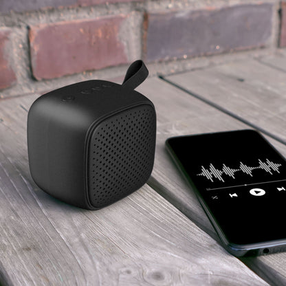 Linocell Trådløs højttaler Sort Bluetooth med vævet rem, set på træ ved siden af smartphone med musikbølge display.