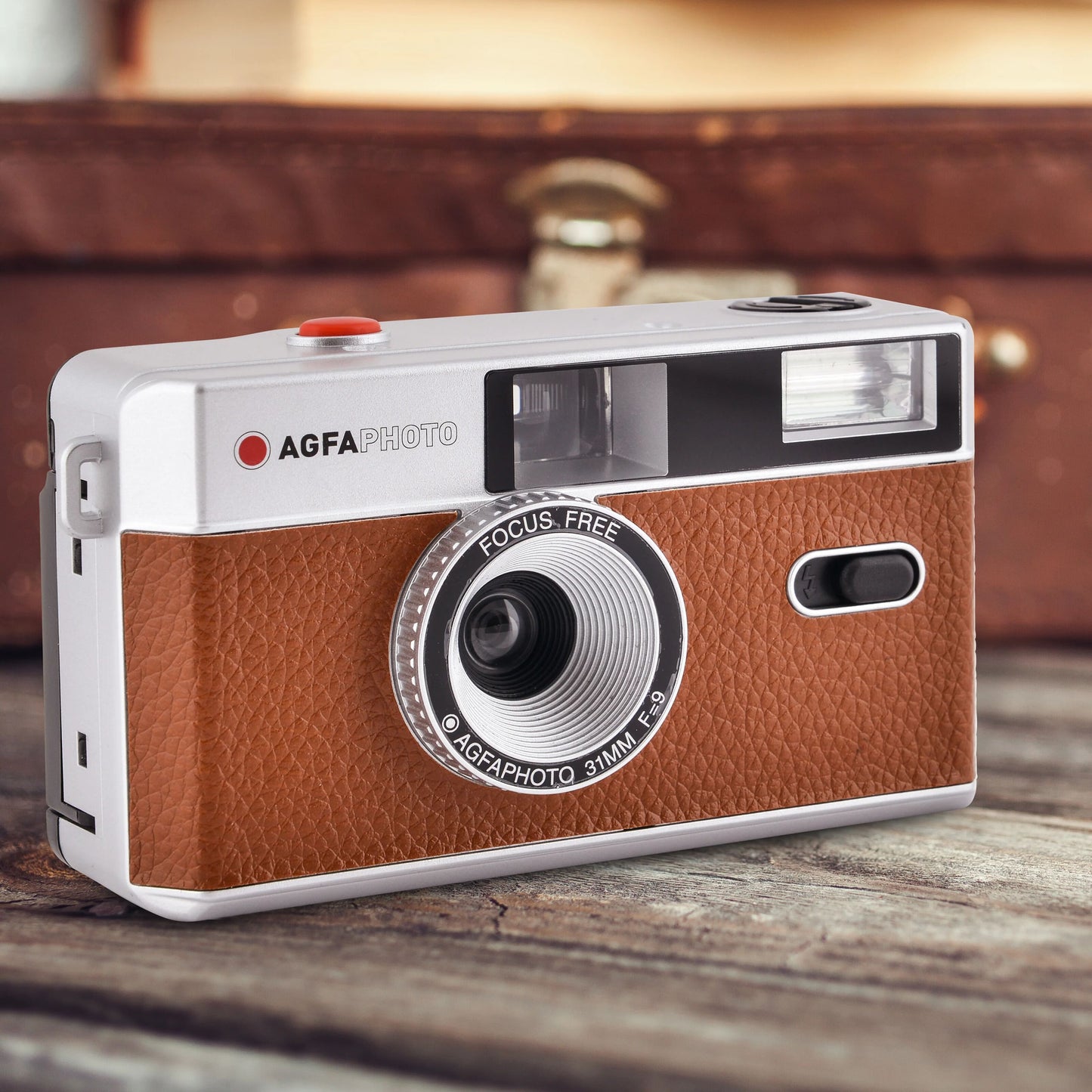 AgfaPhoto Analog kamera 35 mm, brun læderlook, vises på træbaggrund, sløret kuffert i baggrunden.
