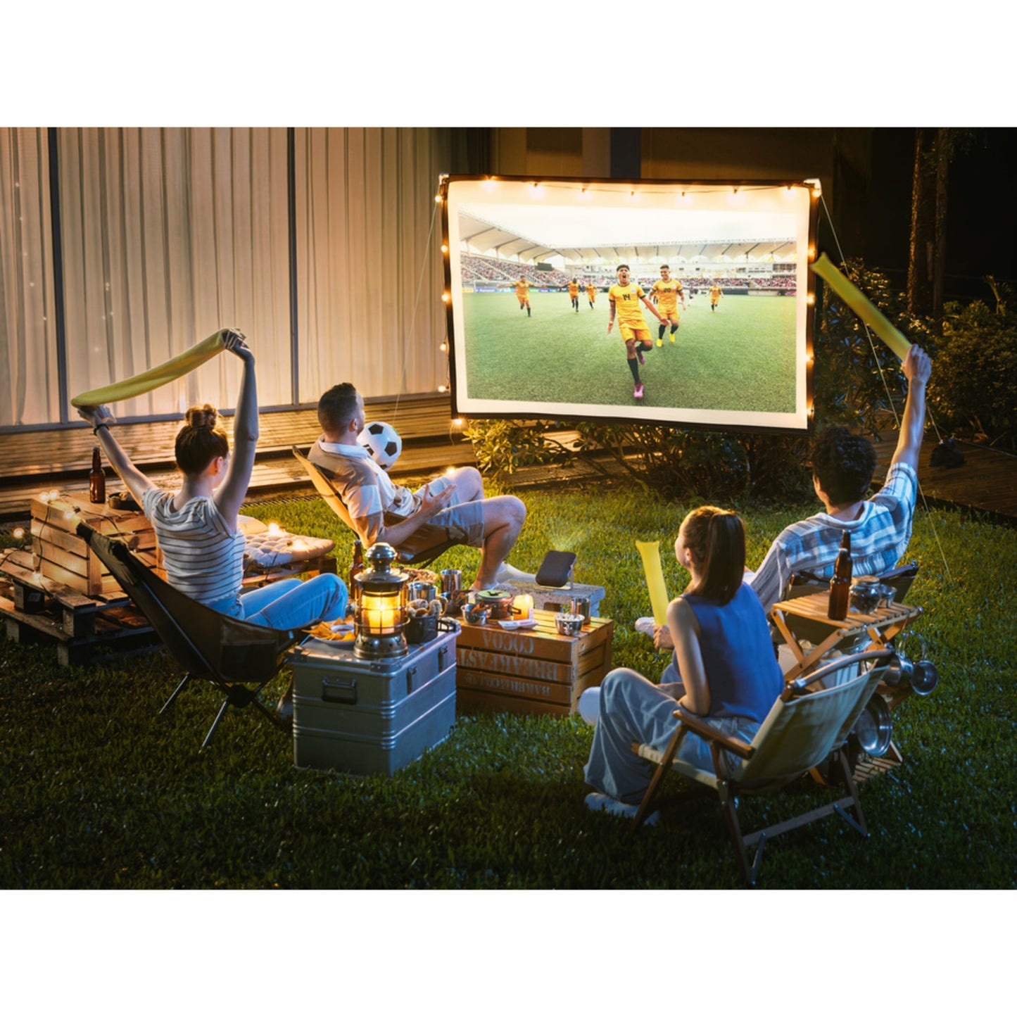 ViewSonic bærbar projektor M1XG med Harman Kardon-højttalere brugt udendørs om aftensmad, snacks og lys i baggrunden.
