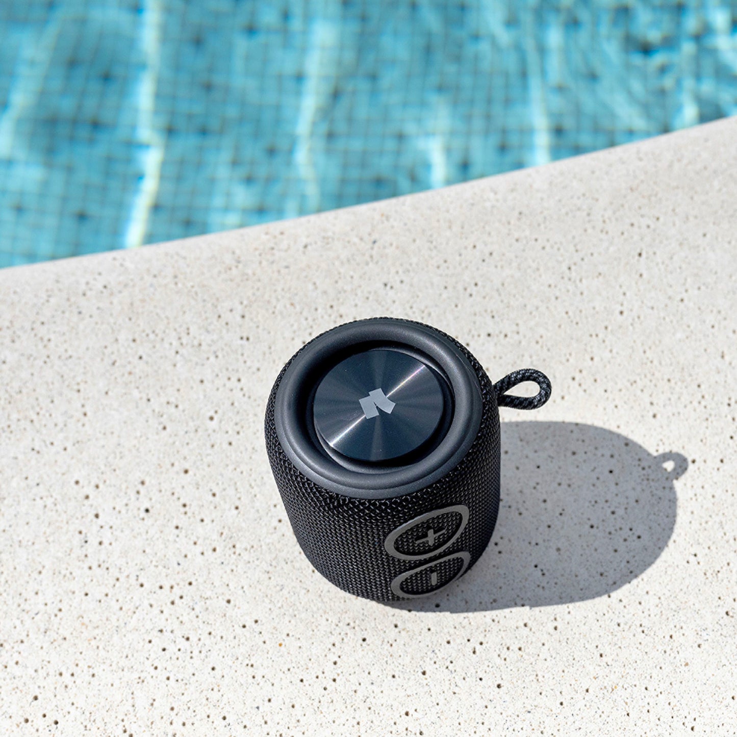 Nomadelic Loud 705 vandtæt Bluetooth-højttaler sort med Bluetooth 5.0 på lys poolkant, blå poolvand baggrund.