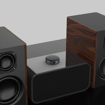 WiiM Mini lydstreamer sort på blank overflade mellem to store trådløse højtalere med sort front, Hi-Res Audio.