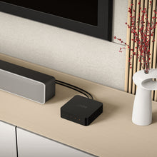 Wiim For lydstreamer sorterer med hi-res lyd ved siden af sølv soundbar på lys hylde.
