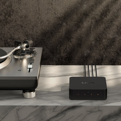 Pladespiller og sort Wiim For lydstreamer med hi-res DAC og multirum ved siden af hinanden på marmorbord, mørk baggrund.