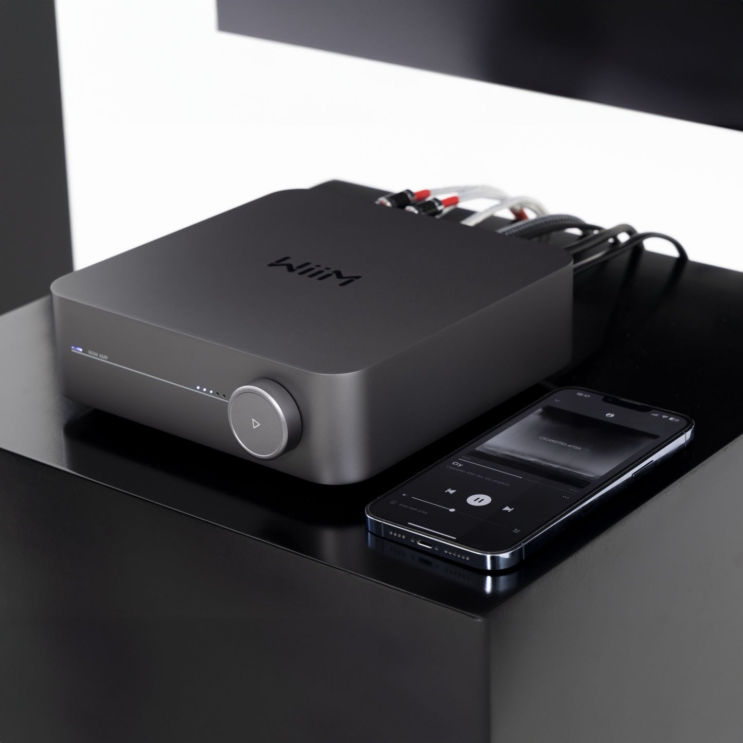 WiiM forstærker med streaming, model Amp Stereo, sort, tilsluttet lydkabler, synlig smartphone med musikafspiller-app.