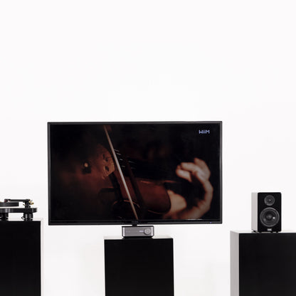 Fladskærms-TV på sort stander med hænder der spiller violin, to sorte højttalere og pladespiller, Wiim Forstærker Amp Stereo.