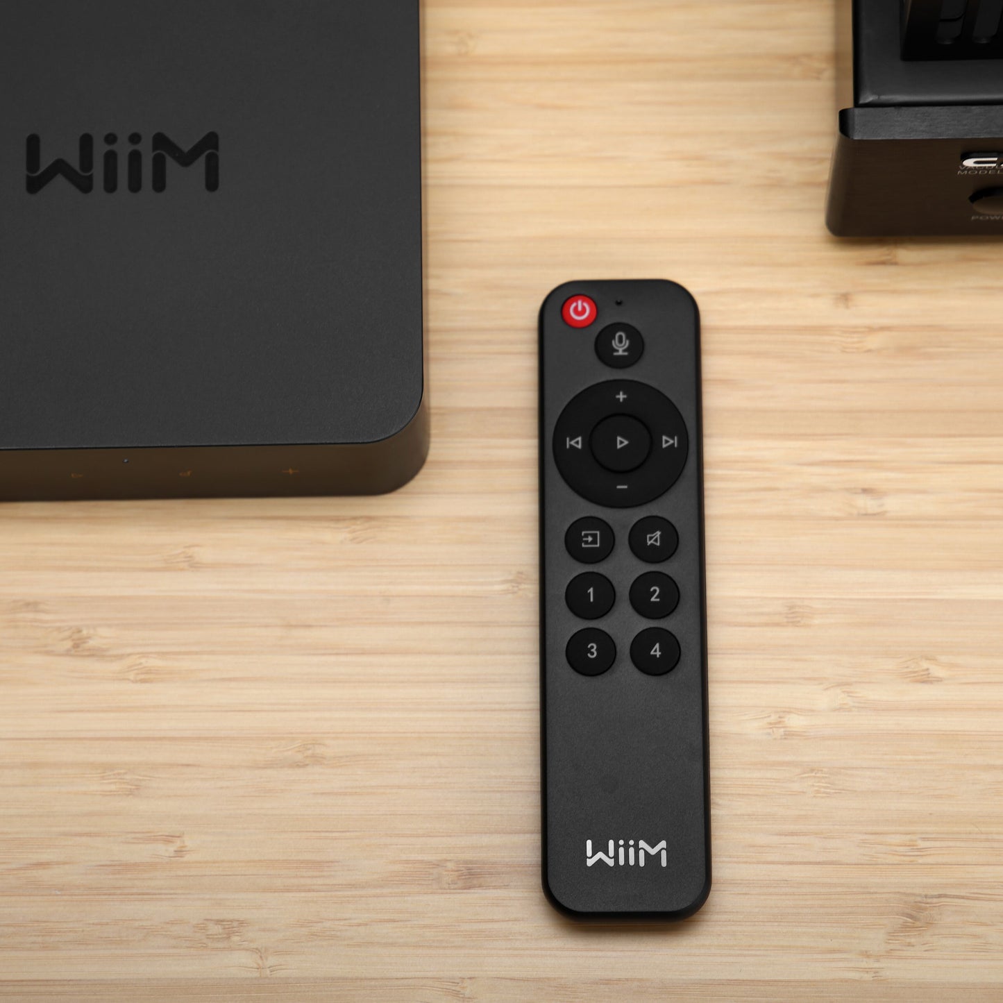 Sort Wiim fjernbetjening til WiiM Mini og Pro ved siden af sort Wiim Pro-enhed på lyst træbord.