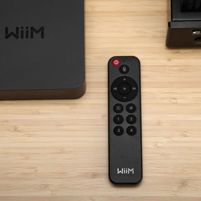 Sort Wiim fjernbetjening til WiiM Mini og Pro ved siden af sort Wiim Pro-enhed på lyst træbord.
