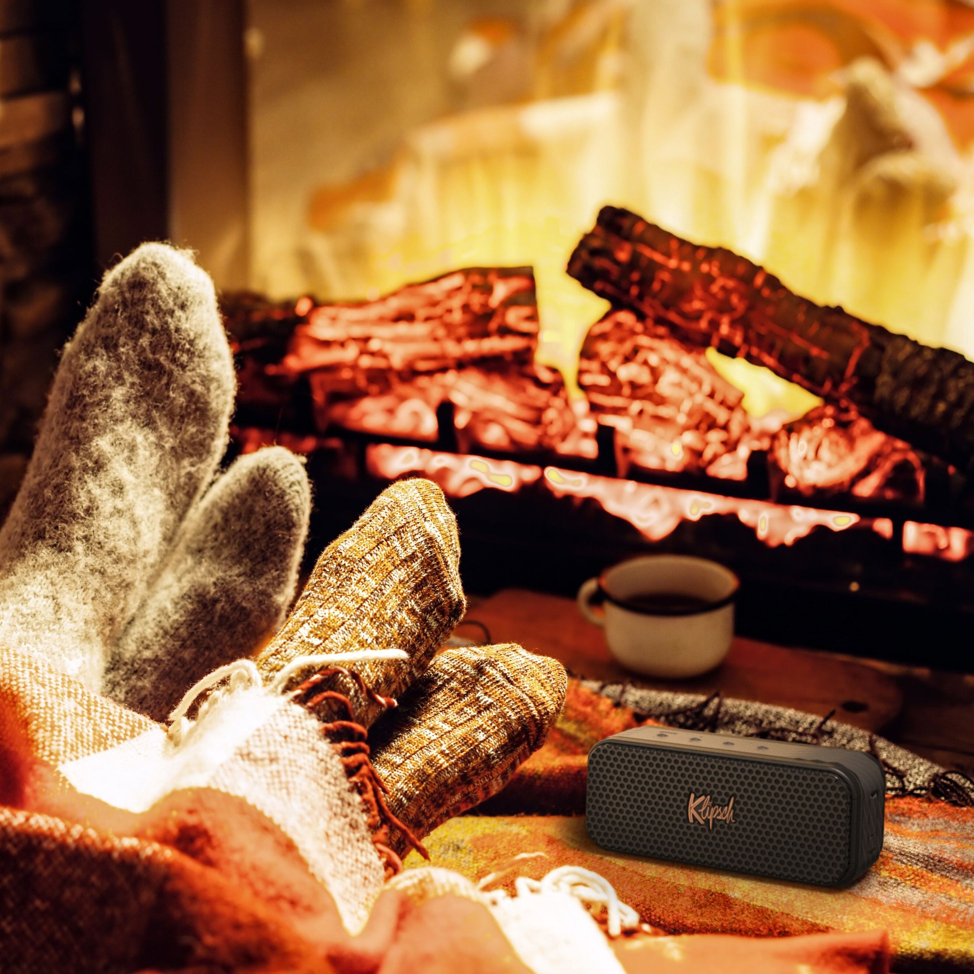 Klipsch Nashville Bluetooth-højttaler sort vises ved pejs, 24 timers batteritid, placeret ved siden af krus.
