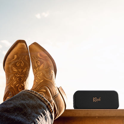 Klipsch Nashville Bluetooth-højttaler med 24 timers batteritid ved siden af lysebrune broderede cowboystøvler på ledge.