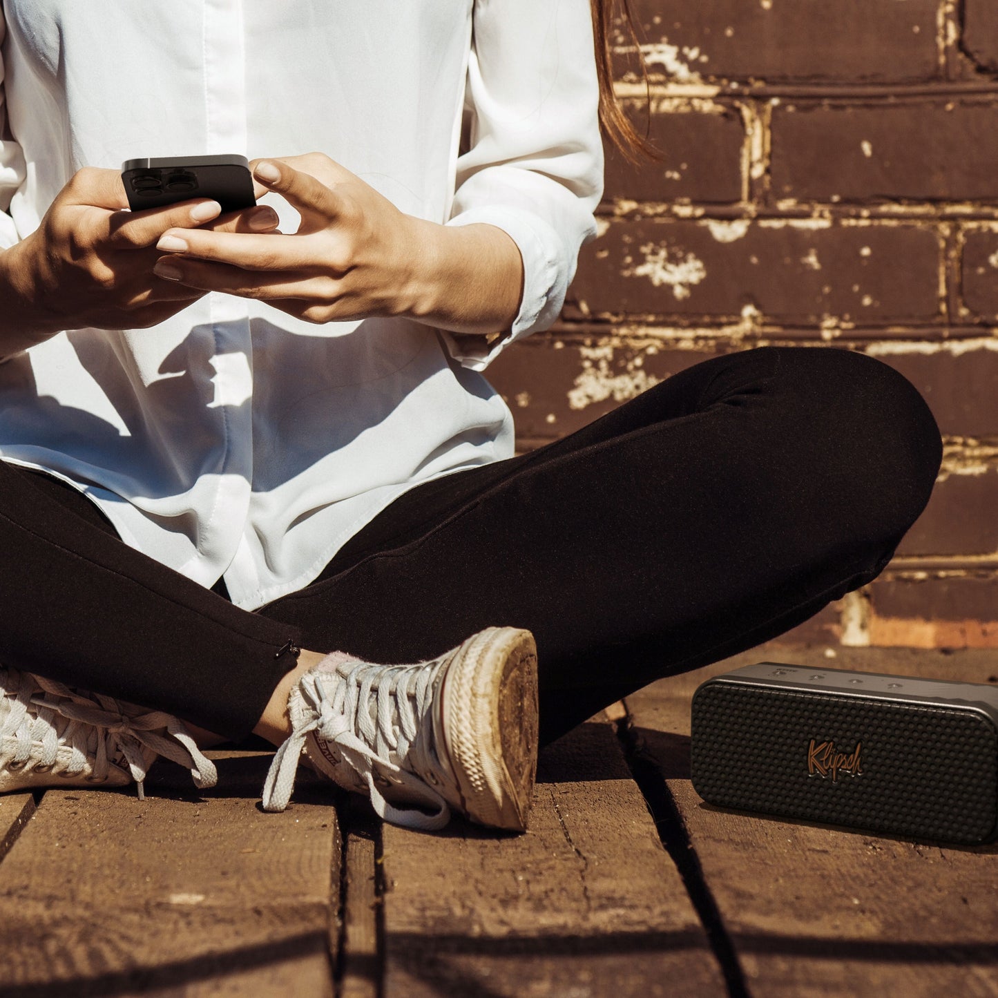 Klipsch Nashville Bluetooth-højttaler sorterer sine ved siden af person med smartphone.