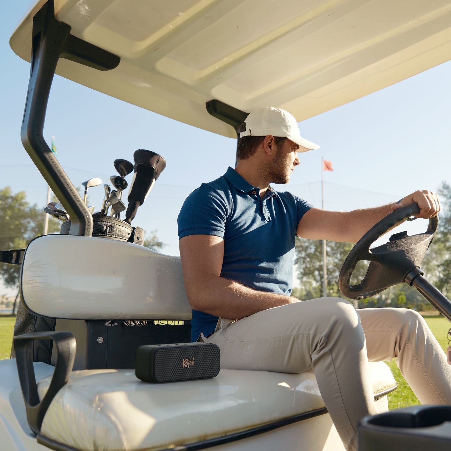 Klipsch Nashville Bluetooth-højttaler sorterer ses på sæde i golfvogn med golfkøller bagved, udendørs kontekst.