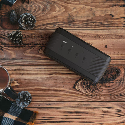 Klipsch Nashville Bluetooth-højttaler sort med op til 24 timers batteritid på træbord sammen med kop, kogler og ternet tørklæde.