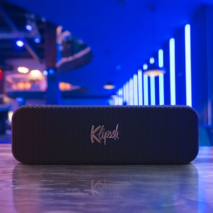 Klipsch Detroit Bluetooth-højttaler sort, synlig på refleksiv overflade med blå og lilla lys, vandafvisende, 20 timers batteri.