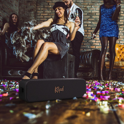 Klipsch Detroit Bluetooth-højttaler sort står på gulv med konfetti i festmiljø, over 20 timers batteritid.