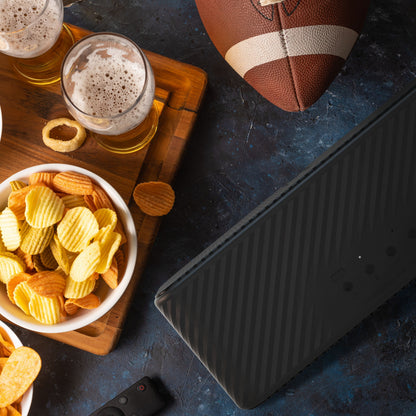 Klipsch Detroit Bluetooth-højttaler sort, 20+ timer batteritid, topview med fodbold, snacks og øl på mørk overflade.