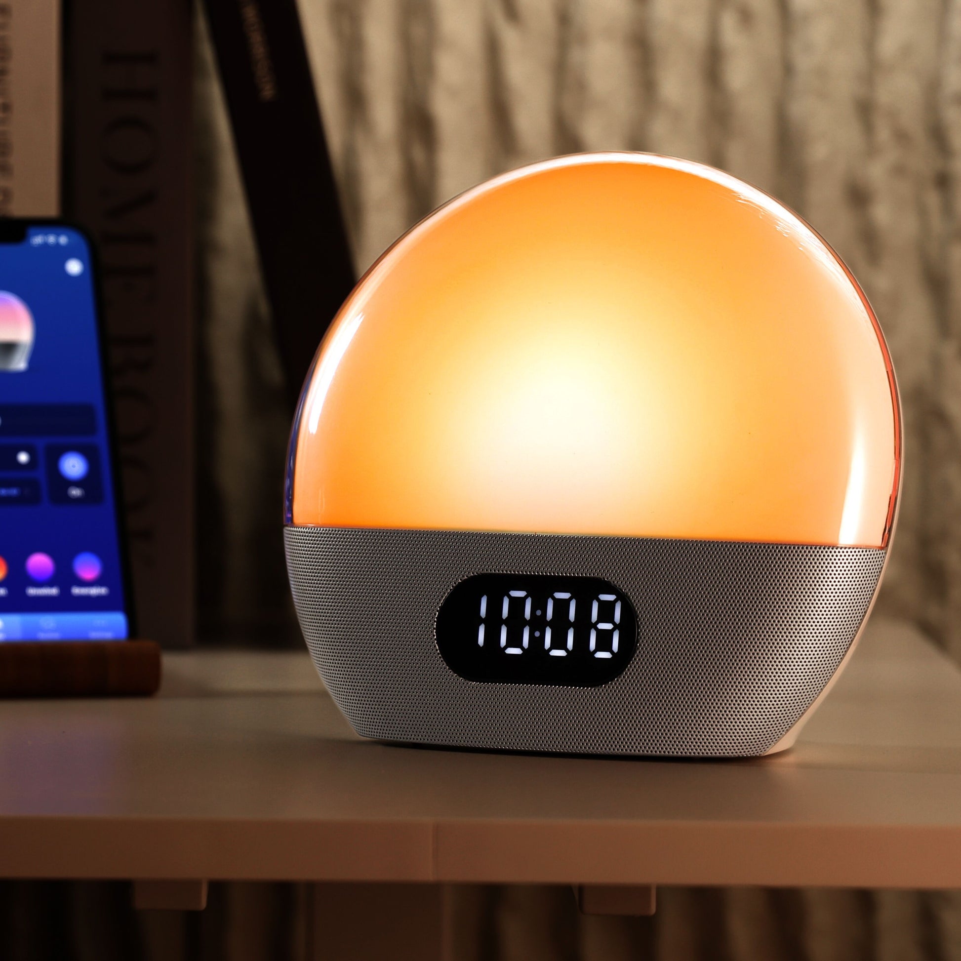 Wiim Vækkeur med wake-up light, solopgangssimulering, orange lys, digitalt 10:08 display ved siden af smartphone og bog.
