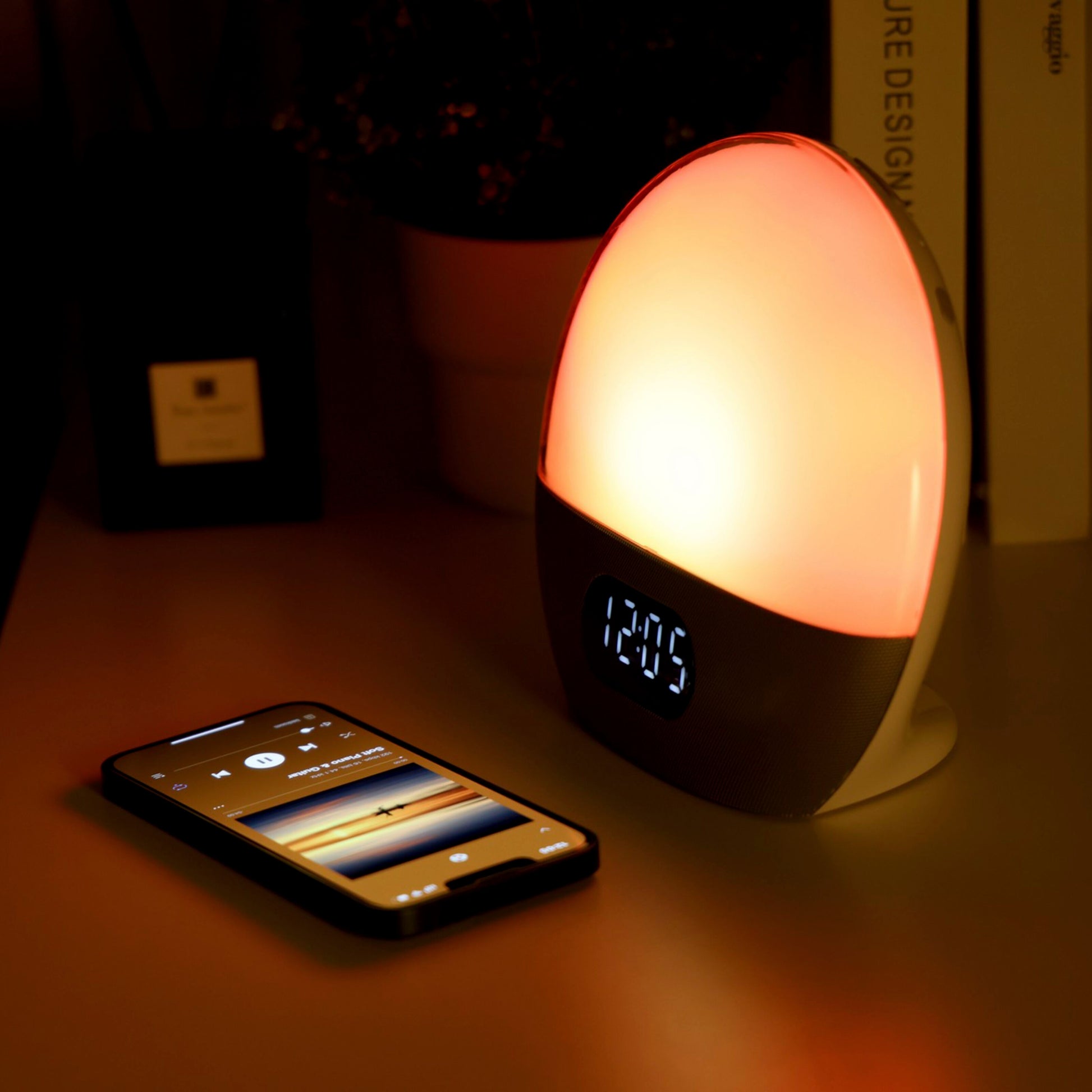 WiiM Vækkeur med wake-up light i orange glød, placeret ved siden af smartphone med musikapp.