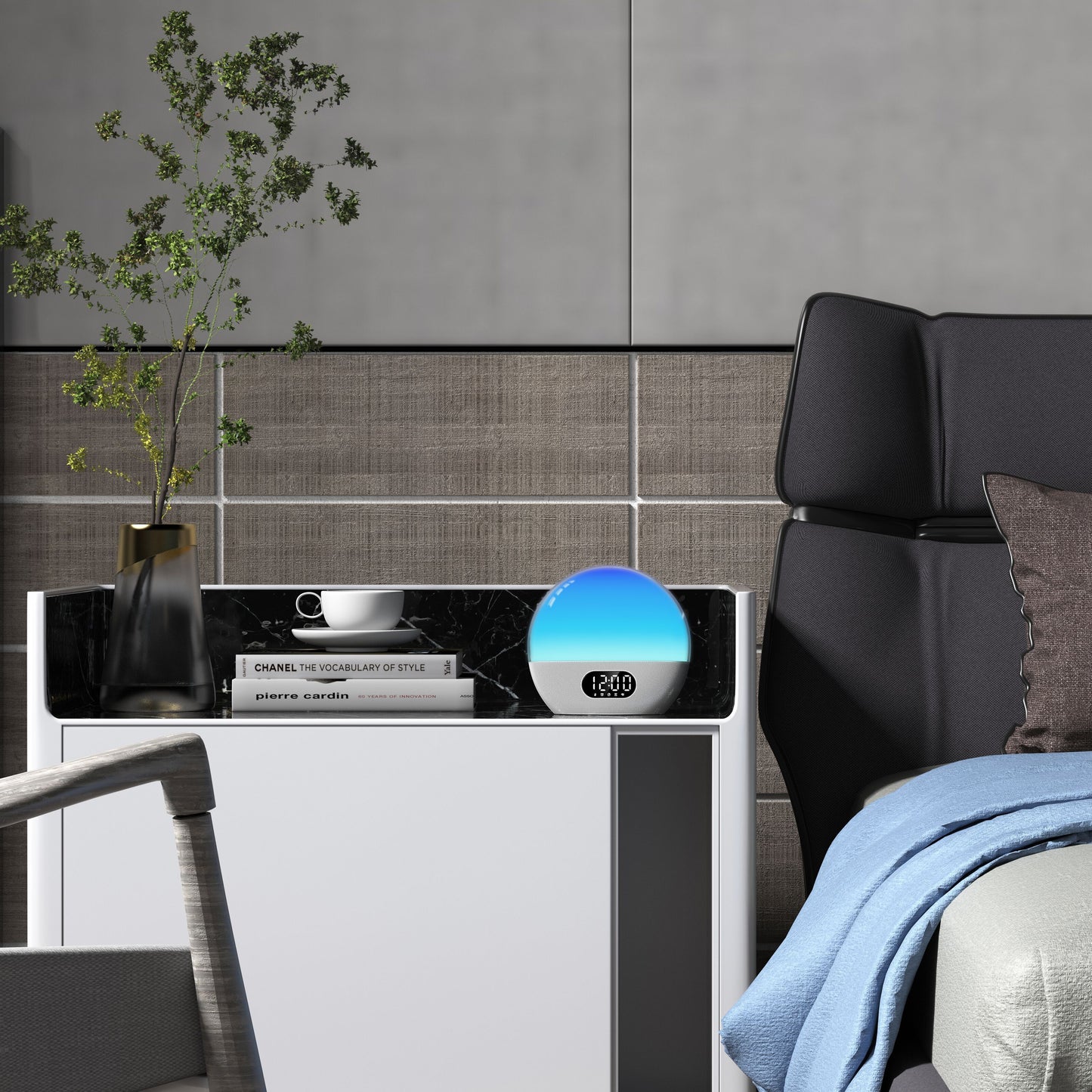 WiiM Vækkeur med wake-up light viser 12:00 på natbord med vase, grønne grene, kop, tallerken og bøger ved seng.