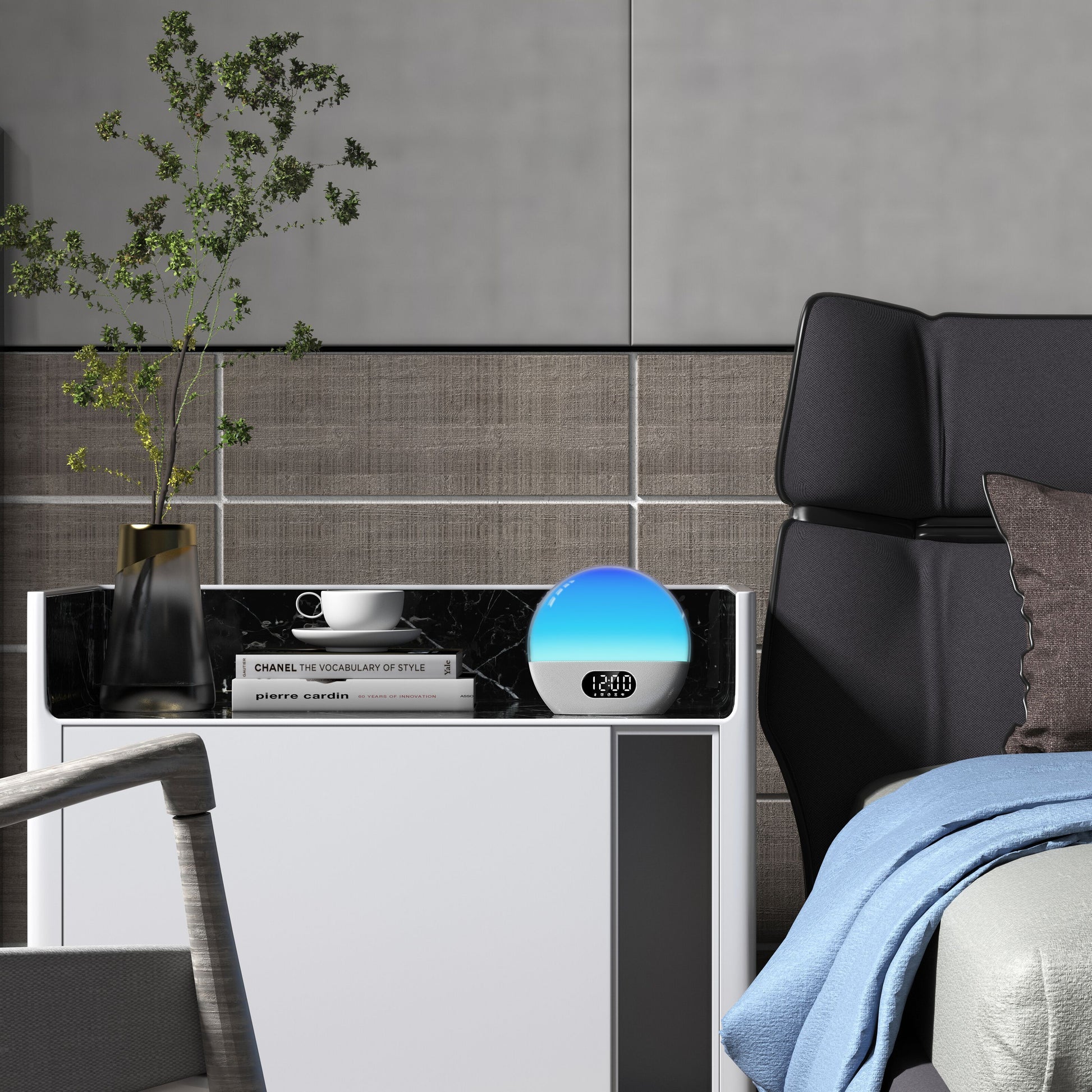 WiiM Vækkeur med wake-up light viser 12:00 på natbord med vase, grønne grene, kop, tallerken og bøger ved seng.