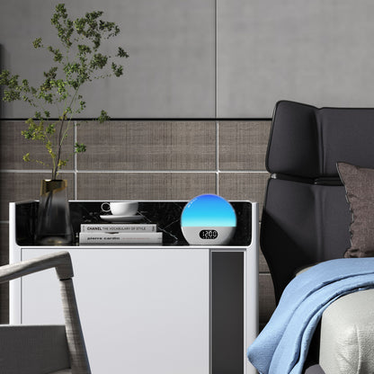 WiiM Vækkeur med wake-up light viser 12:00 på natbord med vase, grønne grene, kop, tallerken og bøger ved seng.