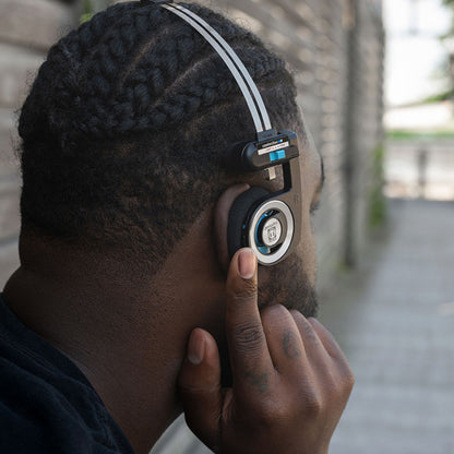 Koss Porta Pro Trådløs 2.0 hovedtelefoner bæres af person med fletninger, finger på ørekop, udendørs.