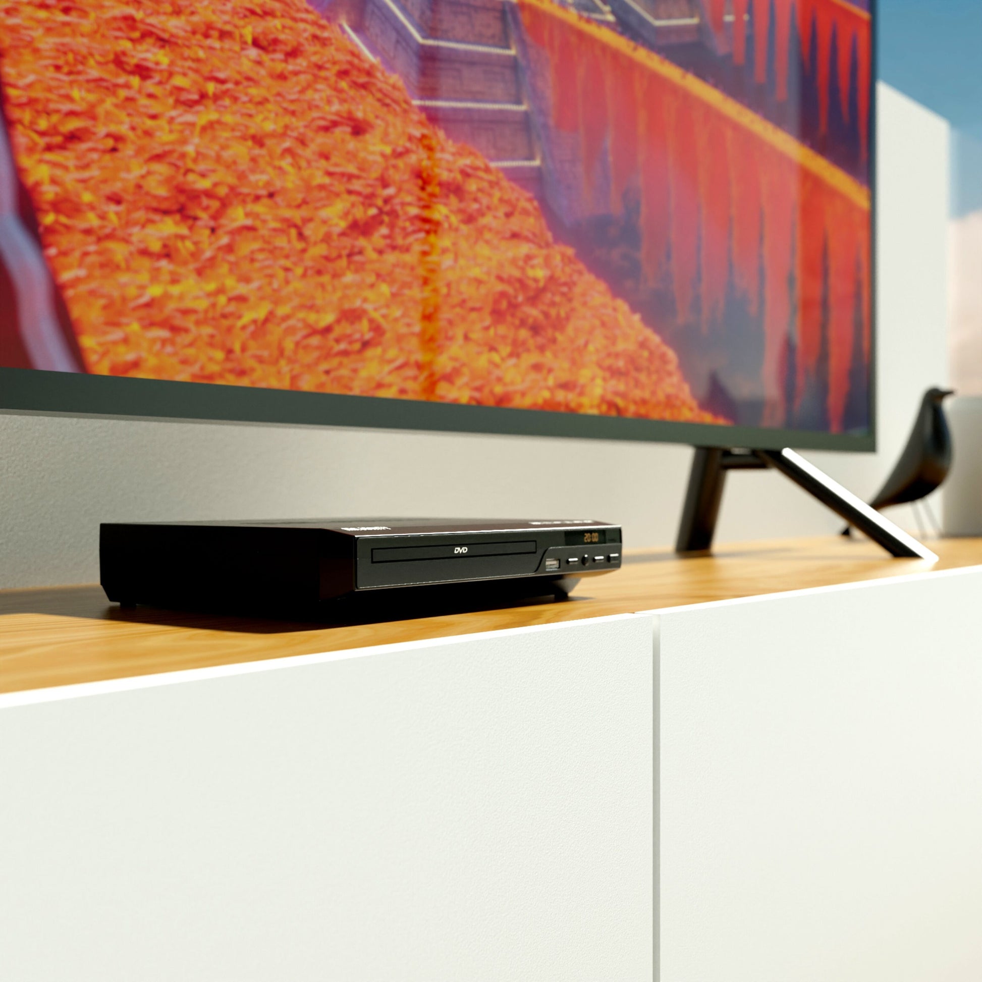 Majority DVD-afspiller med fjernbetjening og HDMI-udgang ved fladskærms-TV på træmediemøbel, skærm med orange/røde toner.