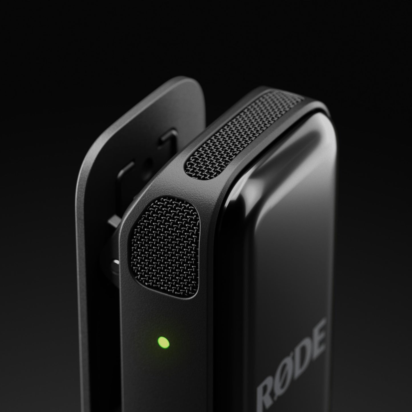 Røde Trådløs mikro lyn transmitter i sort med clip, mesh gitter og grøn indikatorlys mod mørk sløret baggrund.