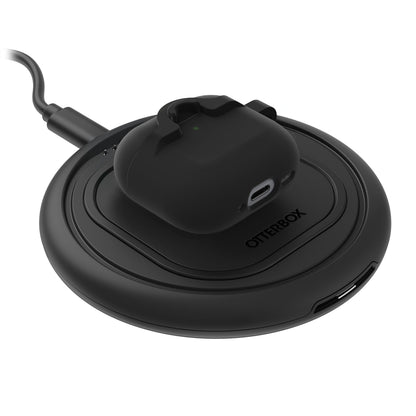 Sort trådløse earbuds i Holdbart cover til AirPods Gen 4 på rund sort Otterbox opladeplade med USB-port og kabel.