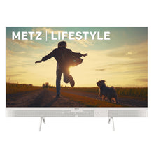 Metz 32" bærbar Google TV, hvid ramme, indbygget soundbar, visning: person hopper på vej med hund solnedgang.